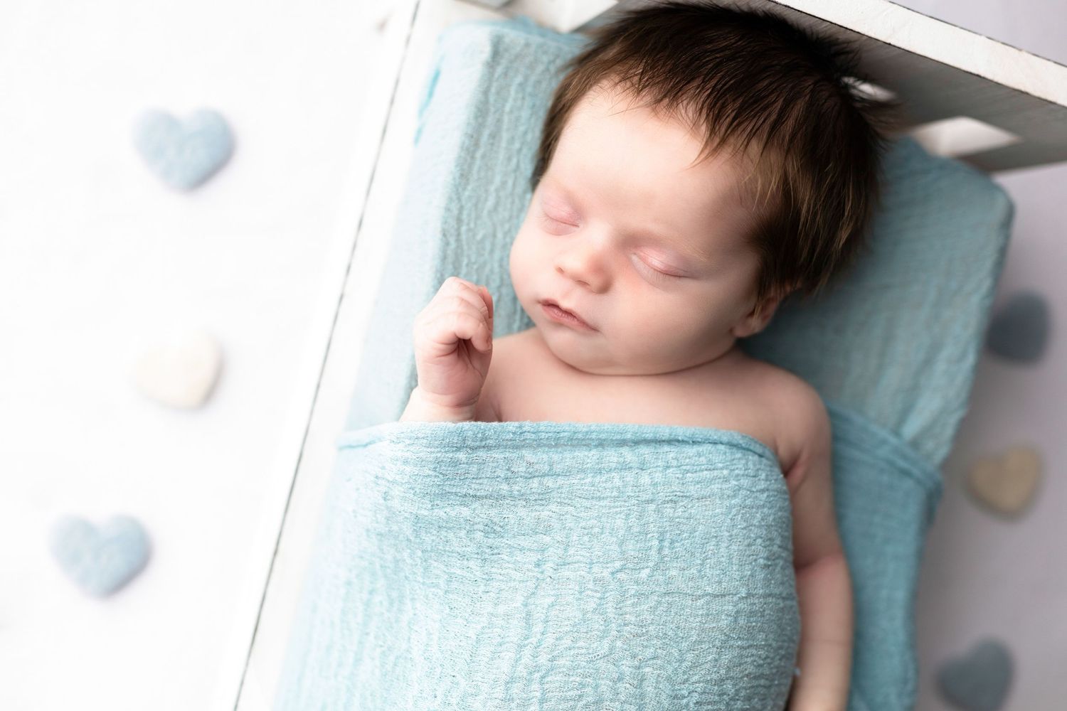 Peaceful sleeping newborn wrapped in soft turquoise blanket in white crib.