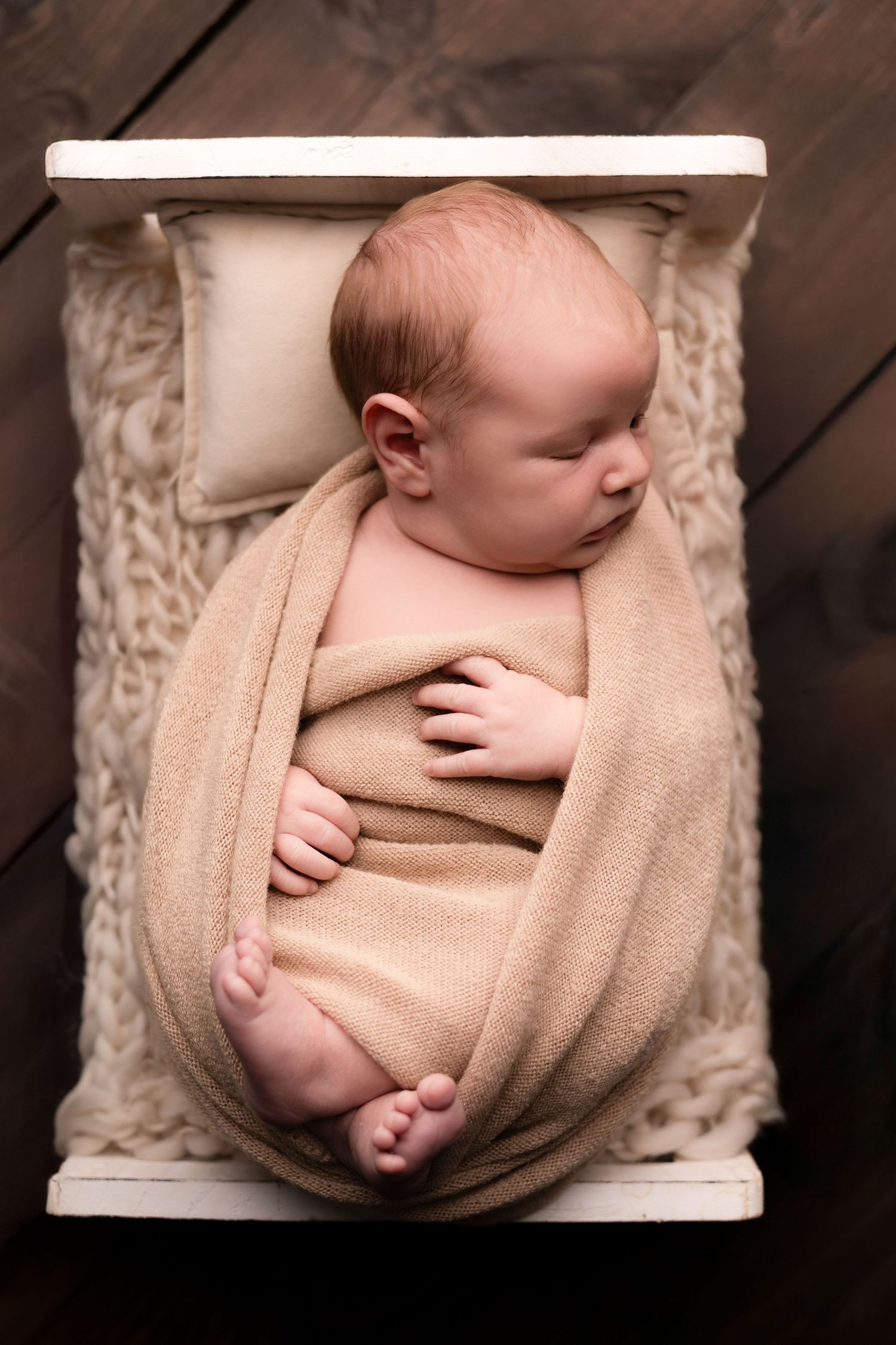Newborn photography featuring soft beige wrapping in wooden box setting.