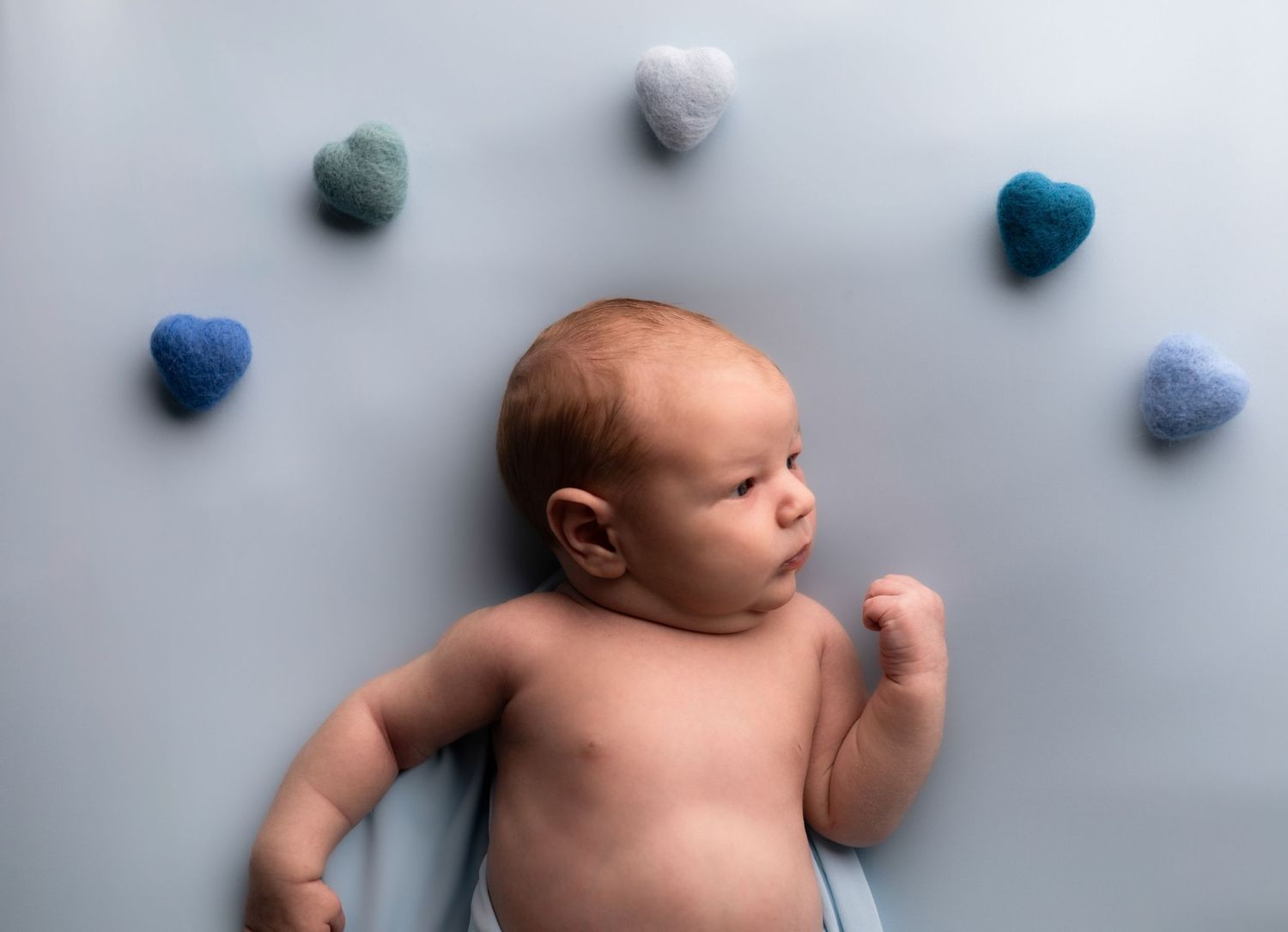 Artistic newborn photo with blue pom pom decorations on light gray background.