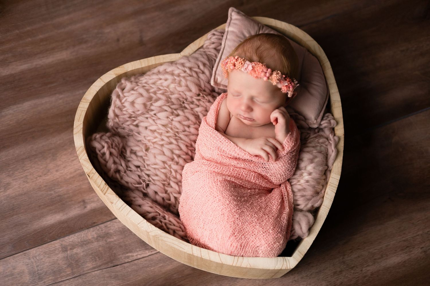 Sleeping newborn wrapped in pink swaddle photographed in heart-shaped basket.