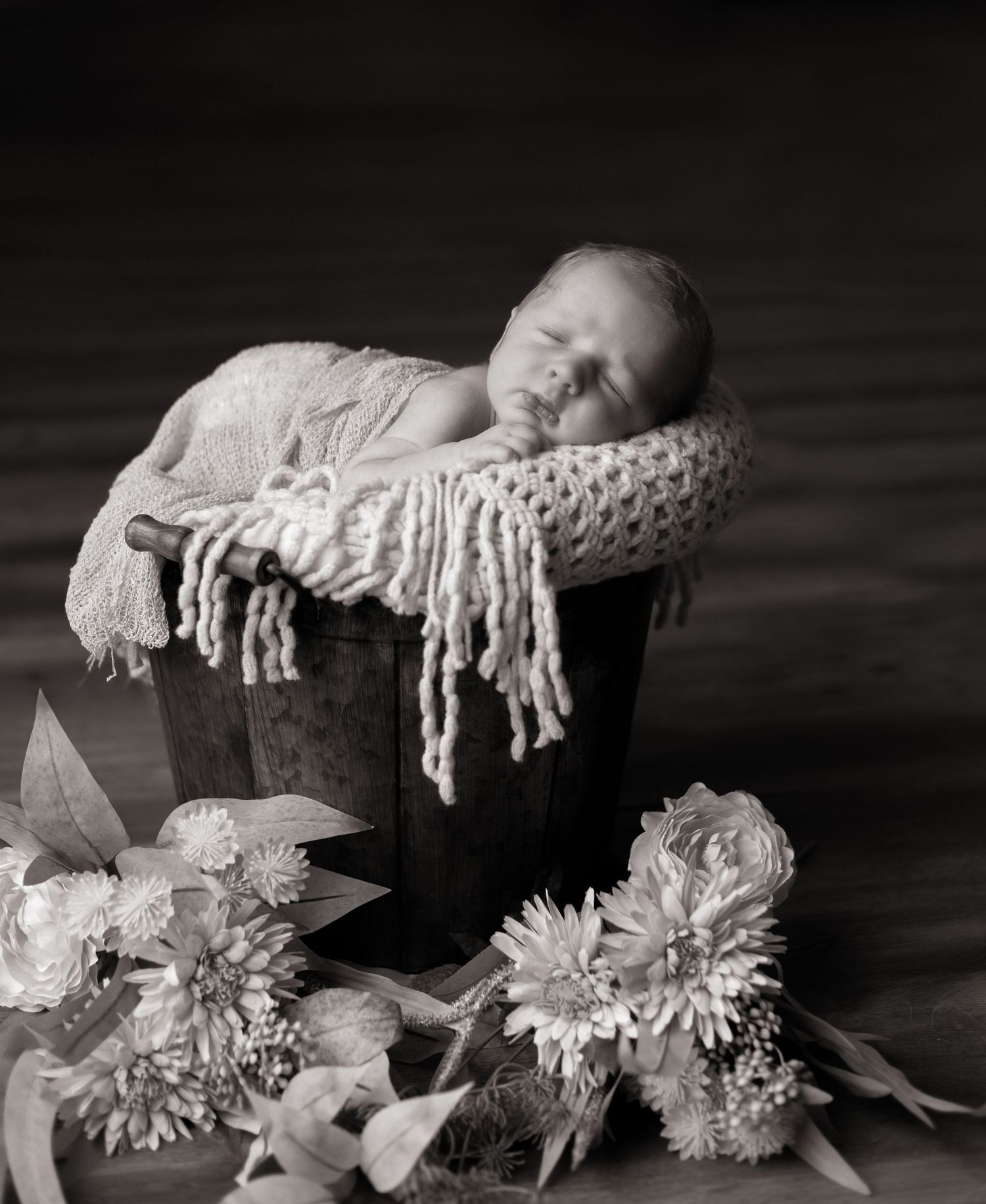 Black and white artistic photo of white flowers and blanket arranged around a wooden box.