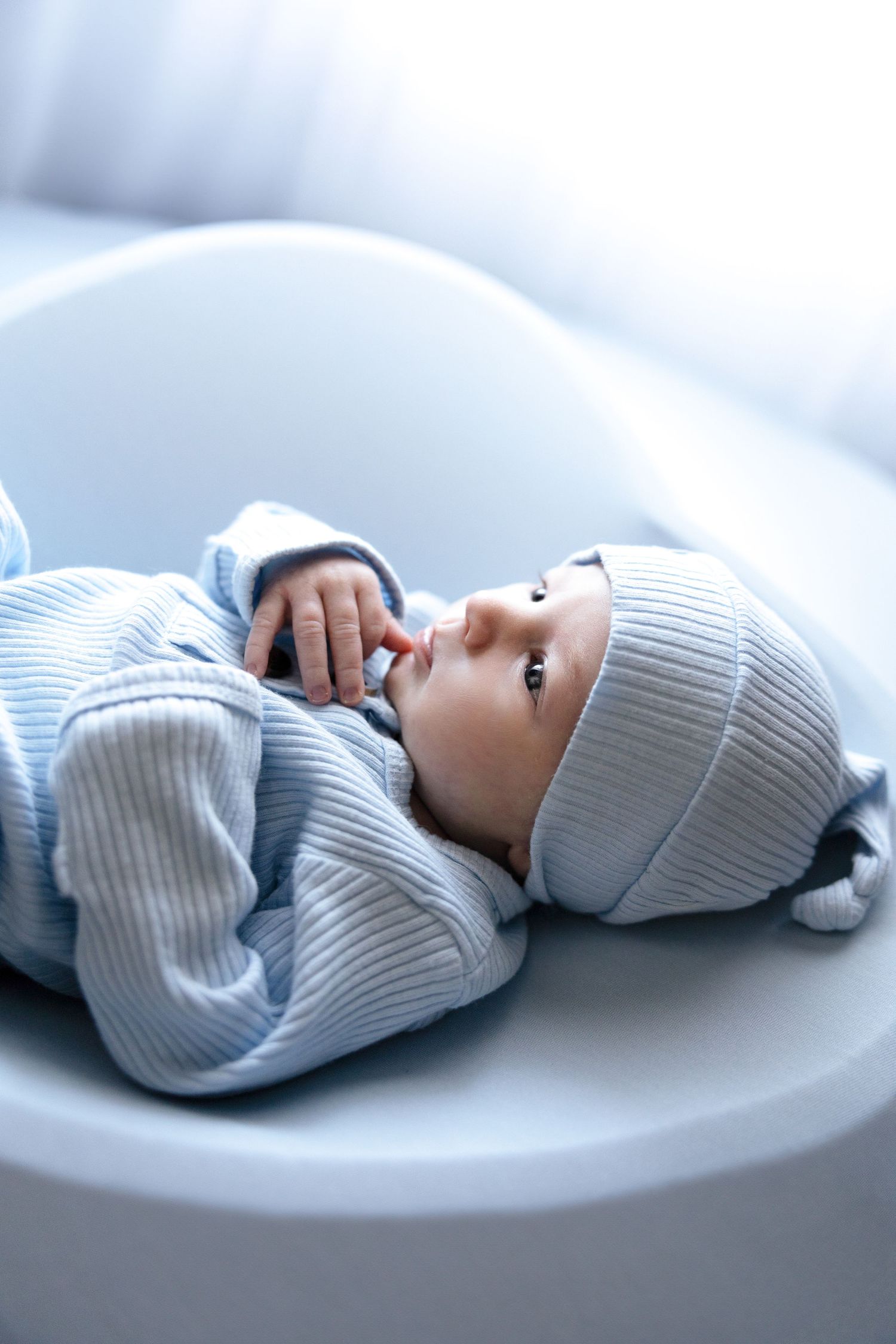 Newborn baby in soft gray knit outfit lying on white blanket shown in multiple poses.