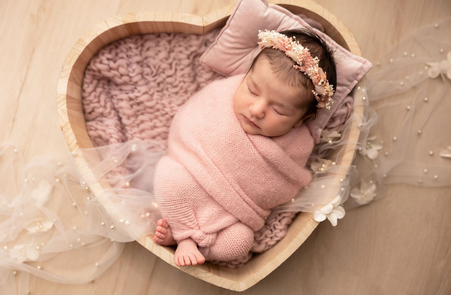 Artistic newborn portrait with soft pink wrapping and ethereal lighting.