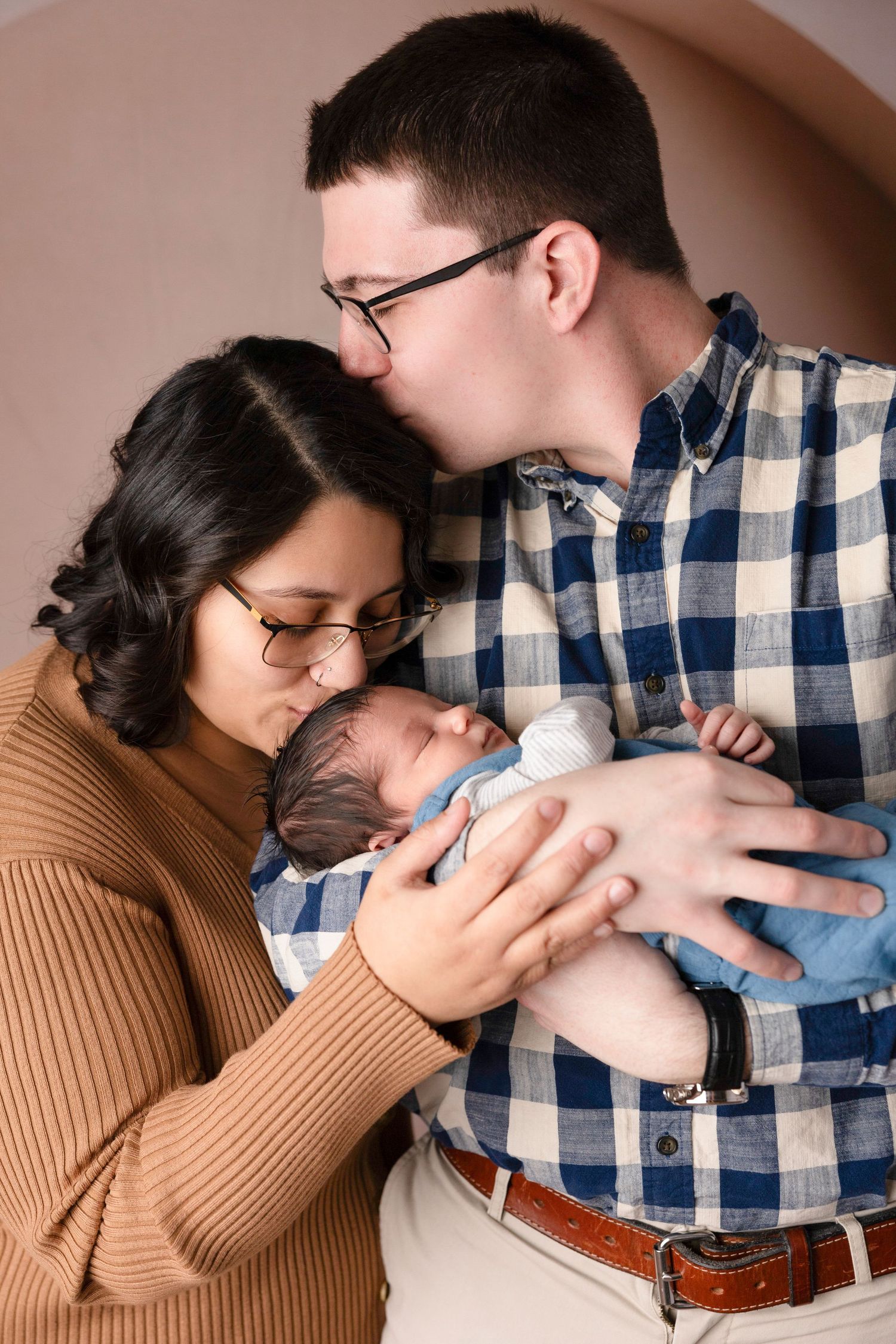 Parents in casual sweaters sharing intimate moments with their newborn in studio setting.