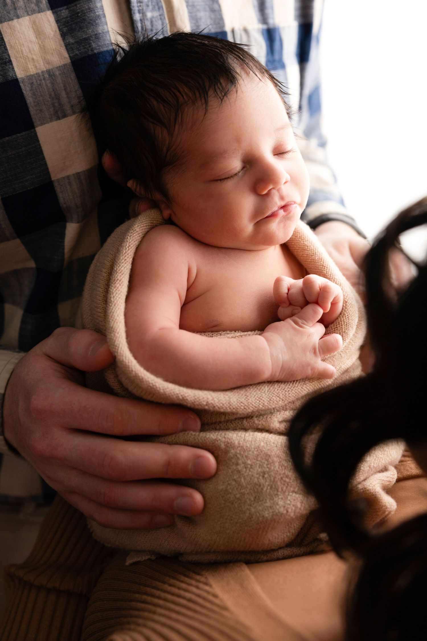 Peaceful newborn sleeping while cradled in soft beige blanket during photo session.