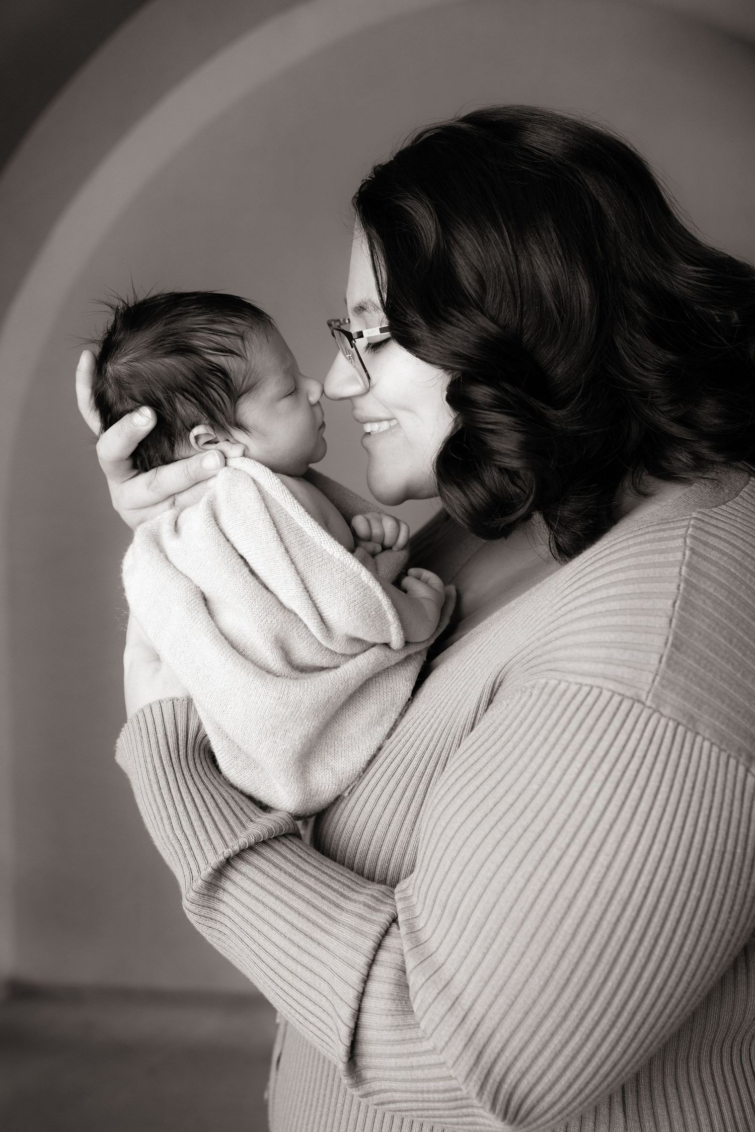 Mother in ribbed sweater holding sleeping baby in tender black and white portrait series.