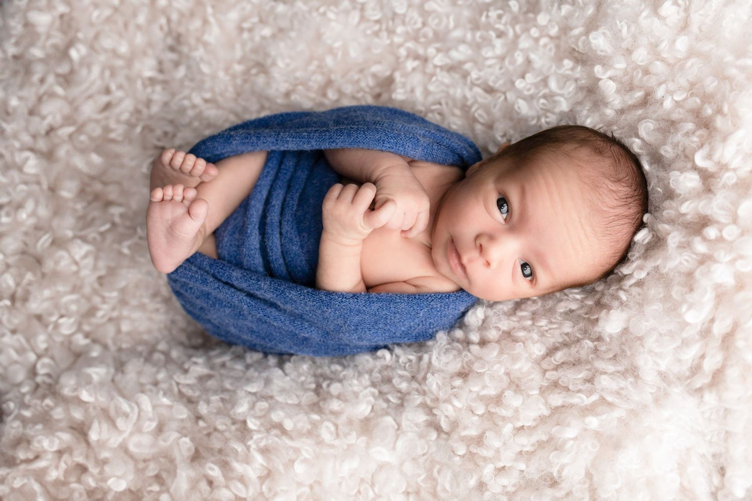 Newborn baby in denim lying on soft textured white backdrop.