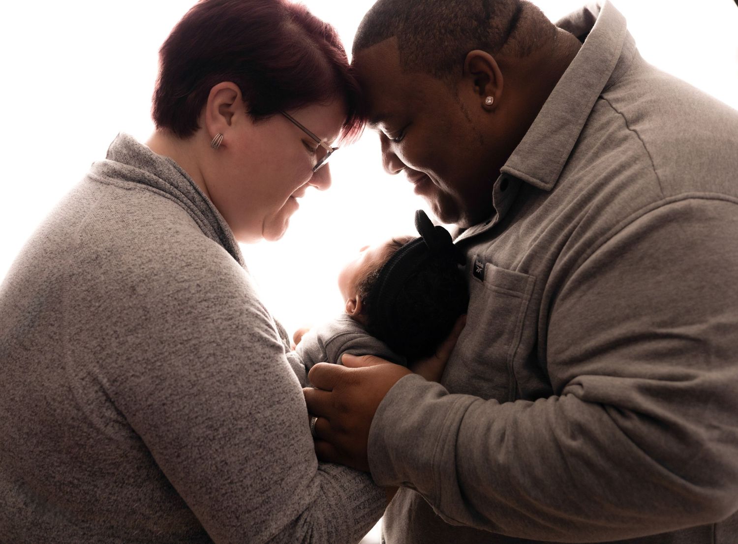 Intimate family moment captured in soft lighting against white background.