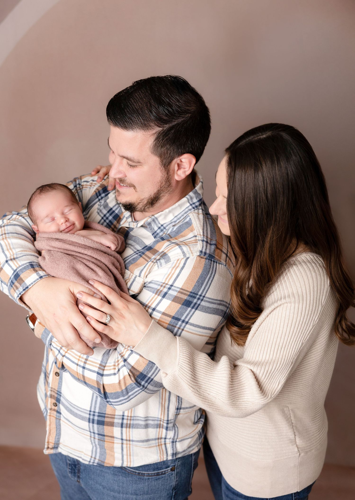 A tender family moment as parents cradle their newborn baby wrapped in a soft blanket.