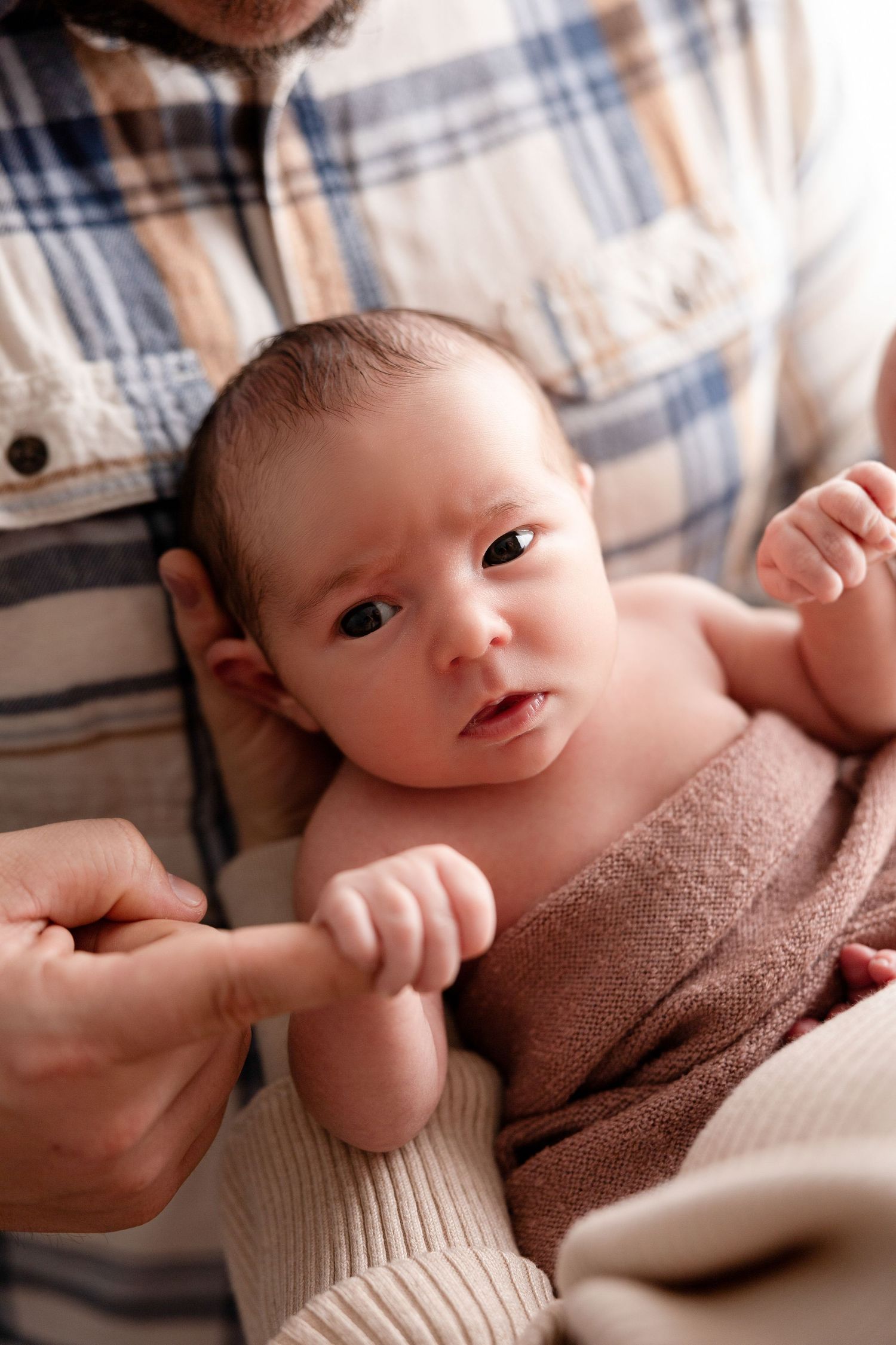 Close-up of a newborn baby wrapped in brown fabric being held by gentle hands.