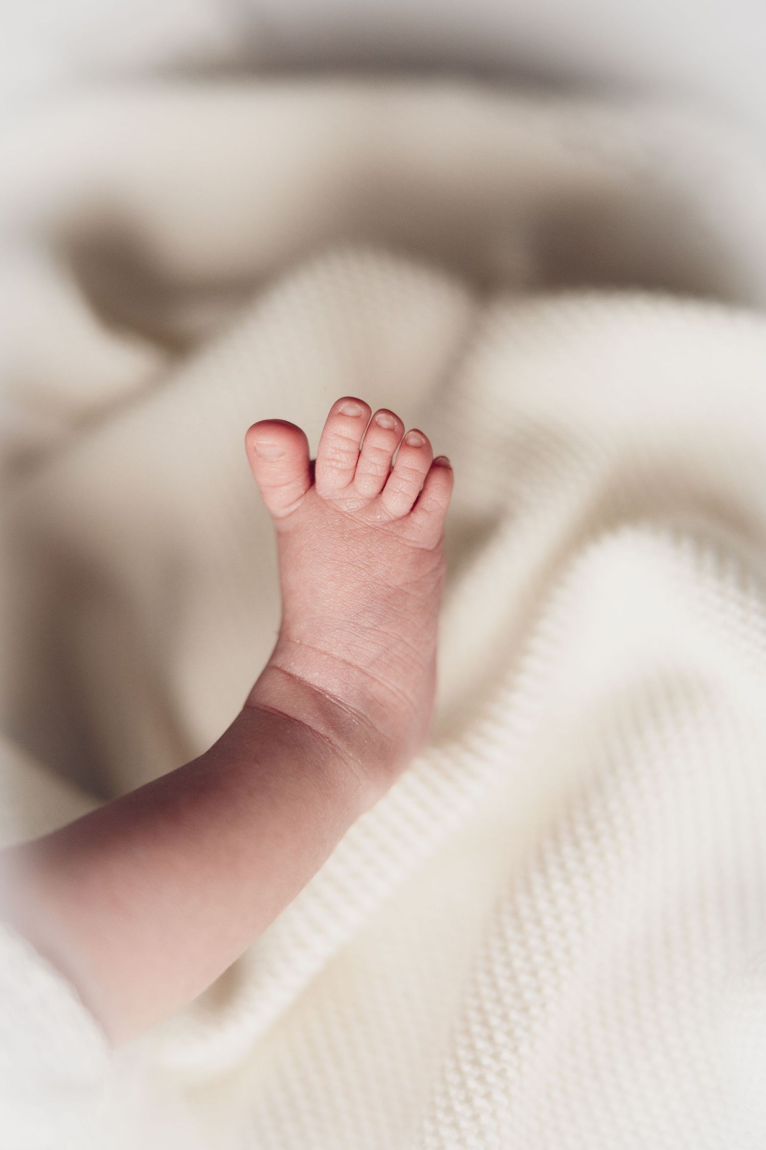 Close-up of a tiny baby foot against soft white bedding.