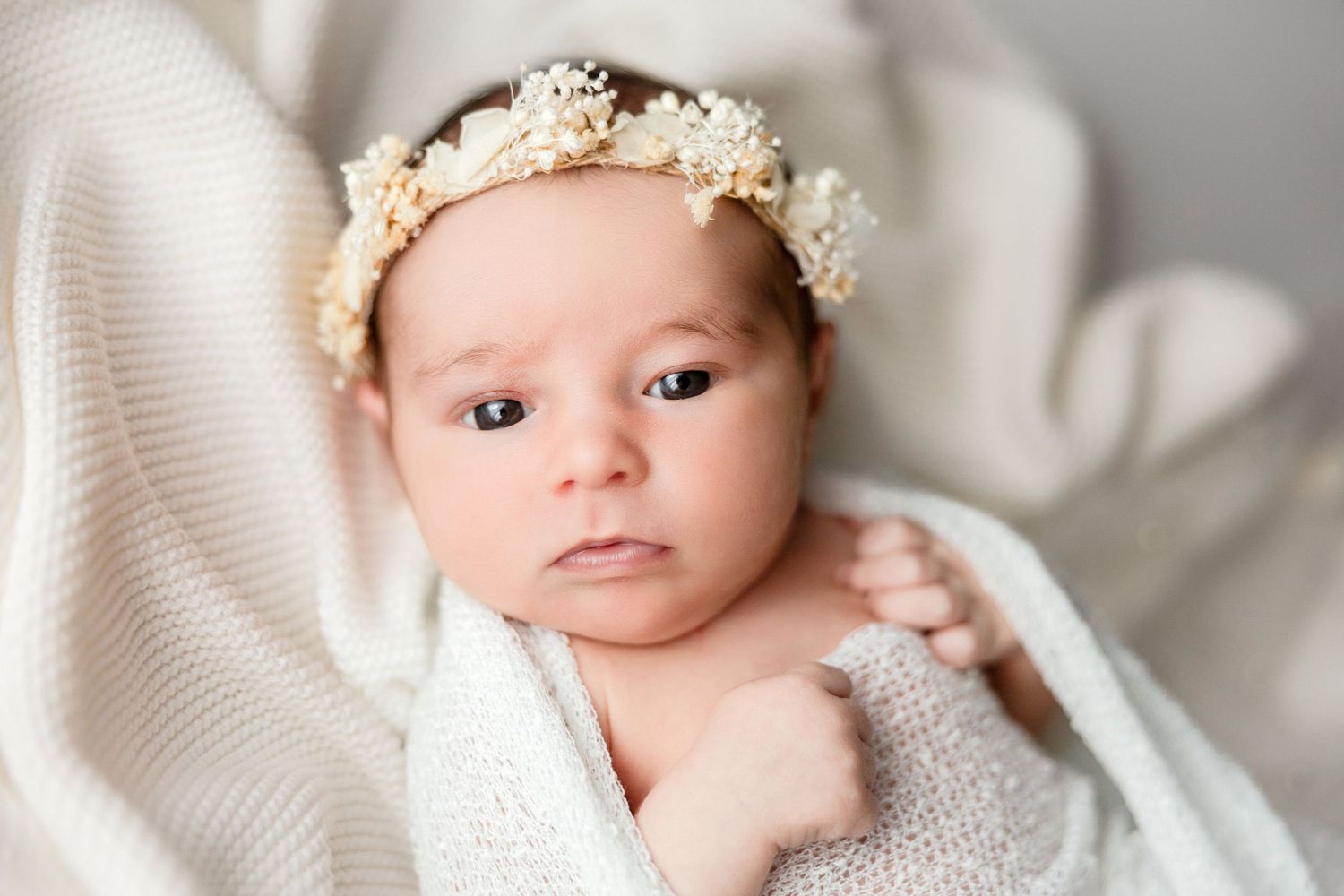 Newborn baby wearing a delicate floral crown while wrapped in white fabric.