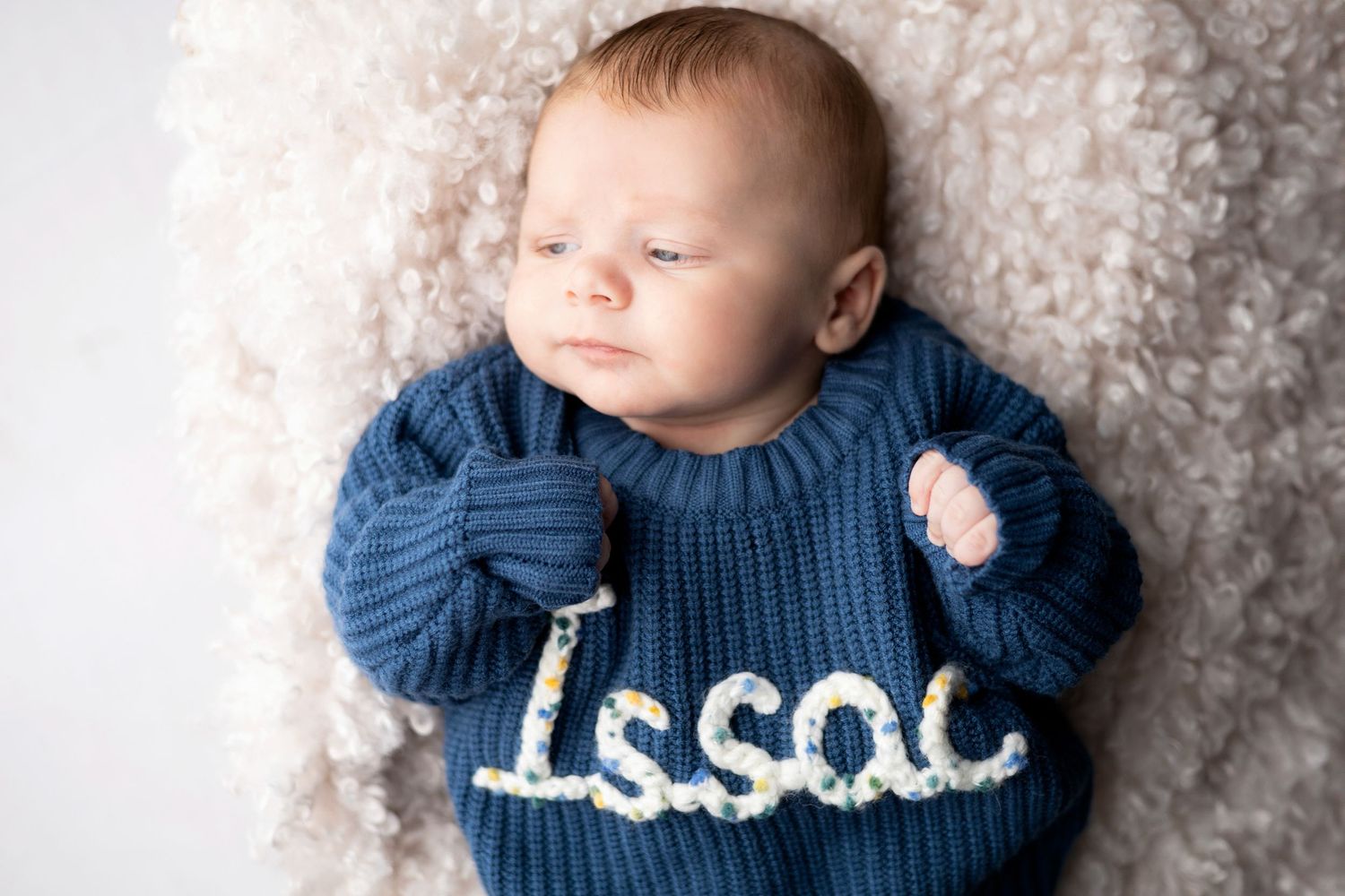 Close up portrait of baby in navy blue sweater against soft textured backdrop.