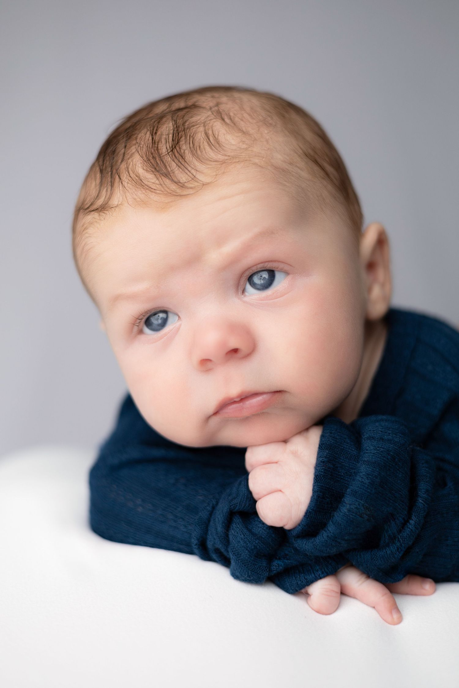 Baby with bright blue eyes laying on white surface wearing dark blue clothing.