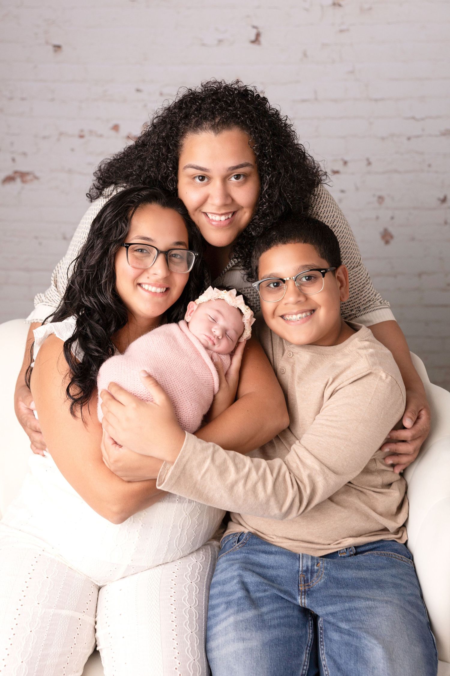 Loving family portrait with newborn baby against white brick wall background.