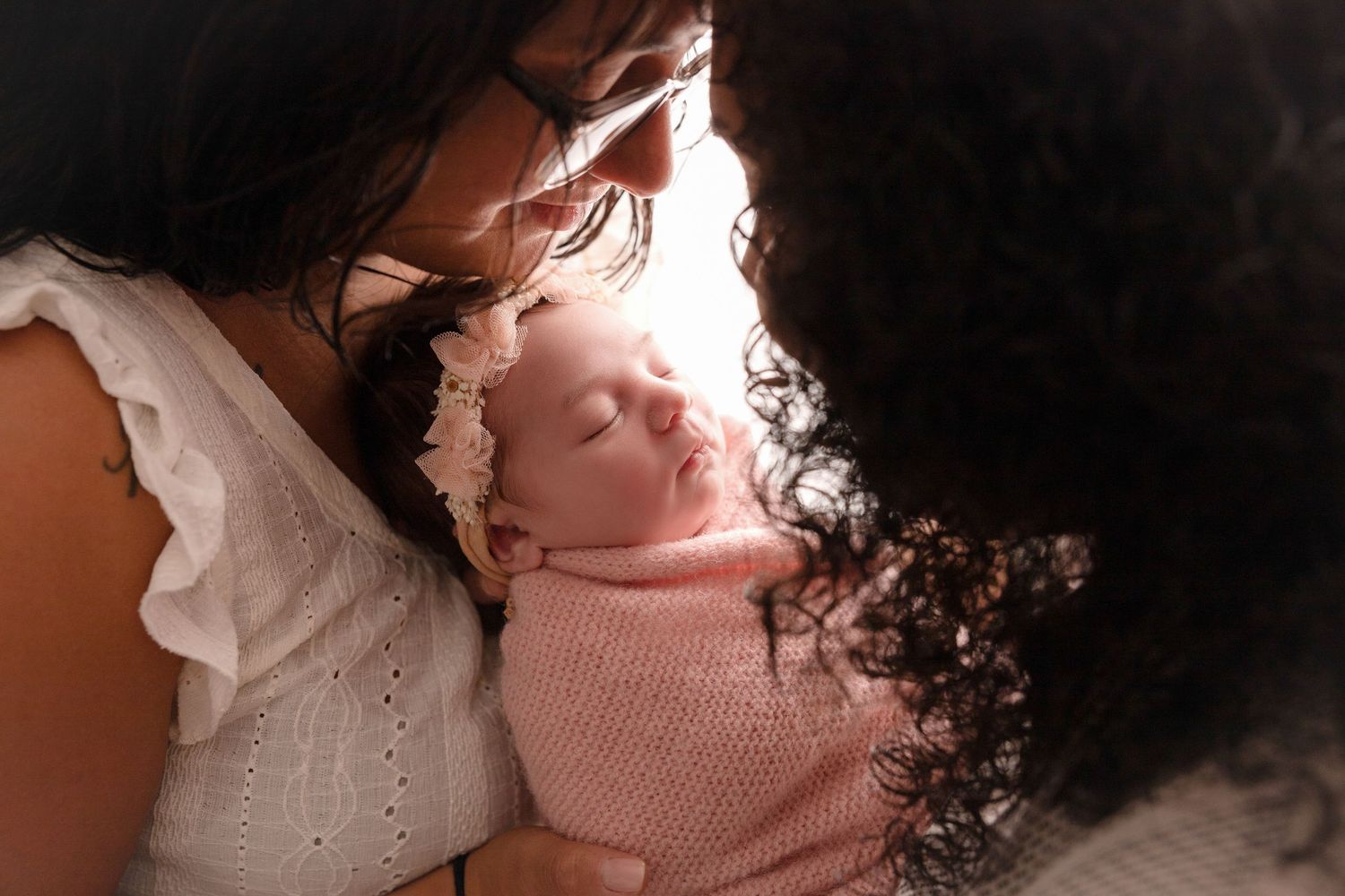 Intimate portrait of newborn baby in pink sweater with soft lighting.
