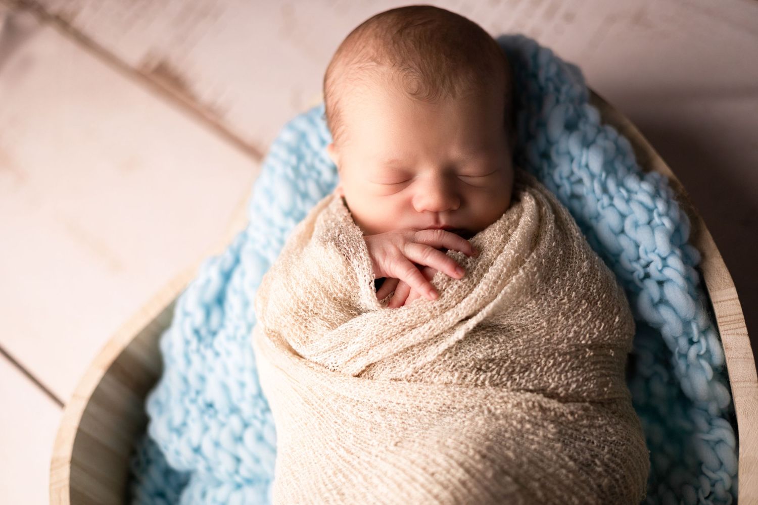 Sleeping newborn wrapped in beige swaddle on soft blue blanket.