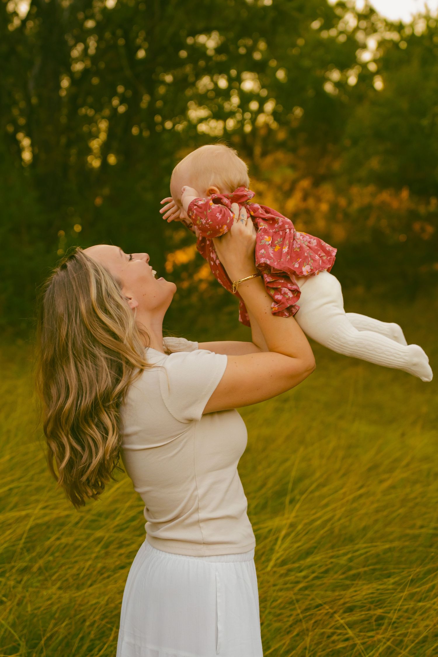 Parent and child playing together in a grassy field during golden hour.
