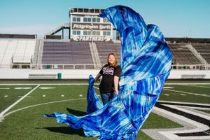 A person stands on a football field as a bright blue fabric billows dramatically in the wind.