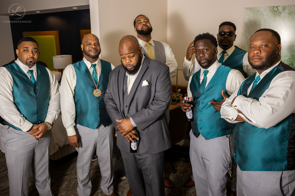 Wedding party members in coordinated teal vests and gray suits posing together.