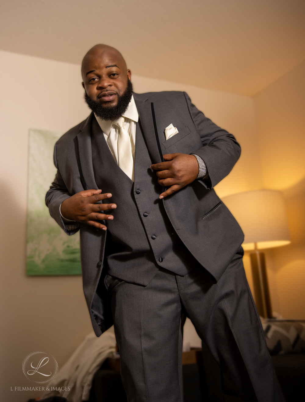 Groom in dark charcoal three-piece suit posing confidently against neutral background.