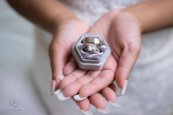 Wedding rings nestled in a gray hexagonal ring box held in open palms.