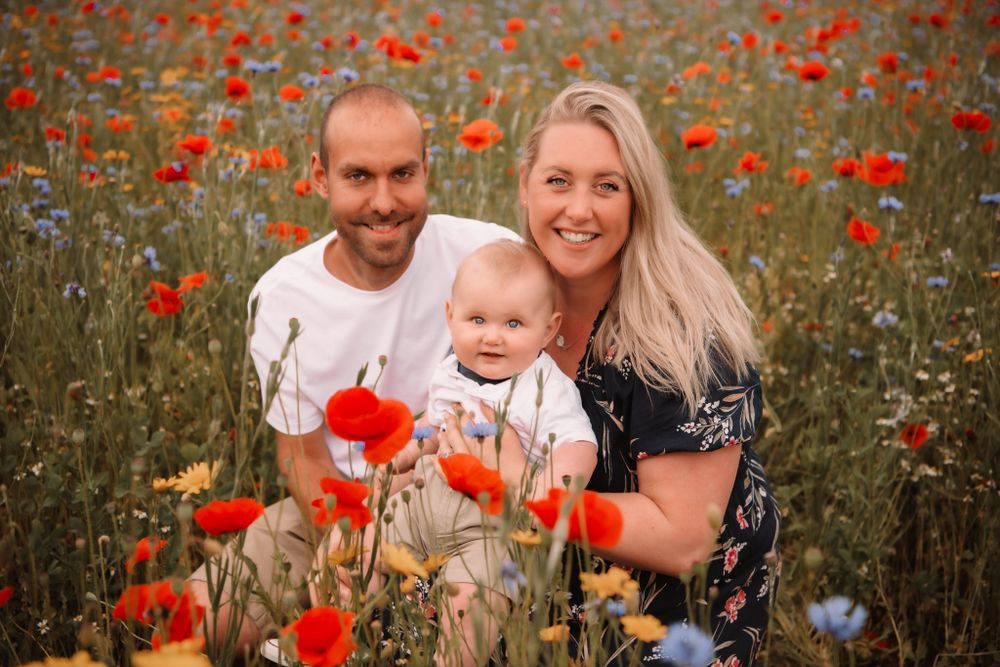 A family poses together in a vibrant field of red poppies during sunset.