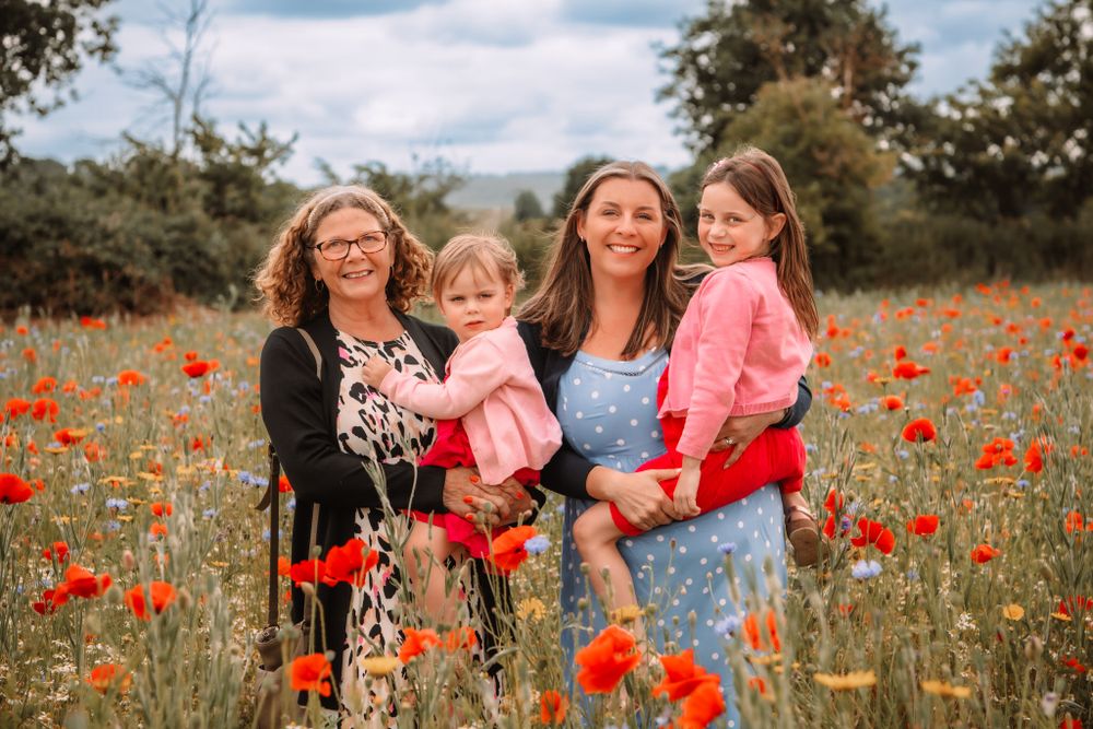 Group stands in a vibrant red poppy field on a sunny day with fluffy white clouds in the blue sky.