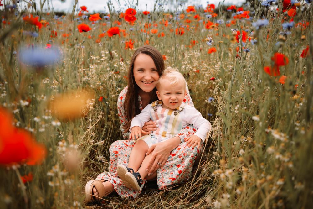 Two people sit together in a vibrant field of red poppies and wildflowers during a summer day.