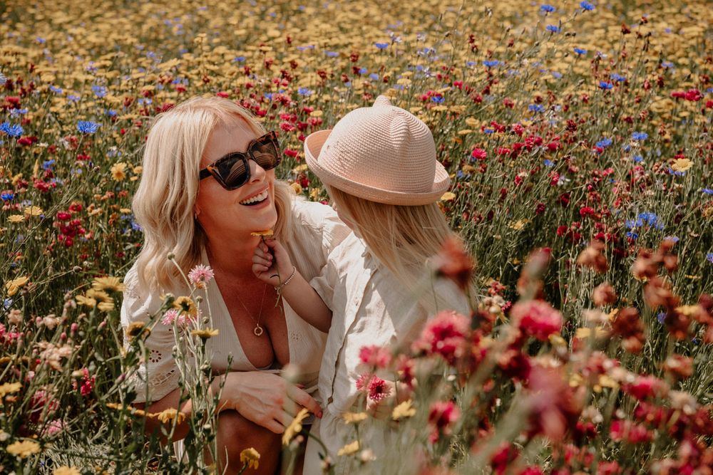 Two people laugh together while sitting in a vibrant field of wildflowers on a sunny summer day.
