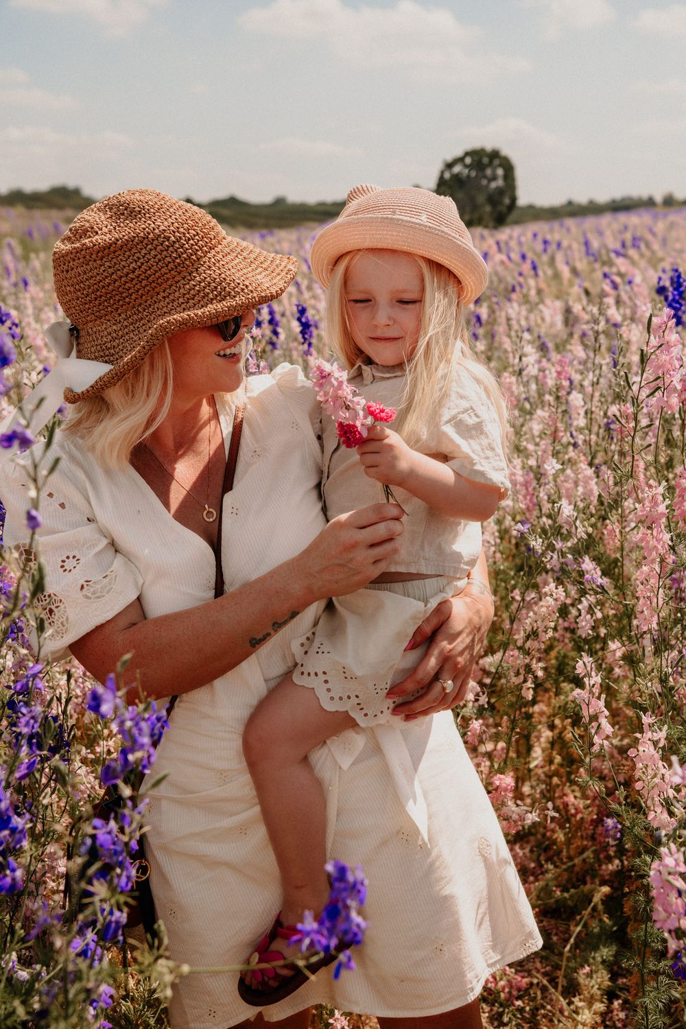 Two people in light colored clothing share tender moments in a blooming wildflower field with purple and white blossoms.