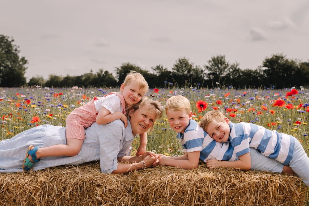 Family of four posing on a hay bale in a vibrant poppy field, smiling and enjoying a sunny outdoor photo session.