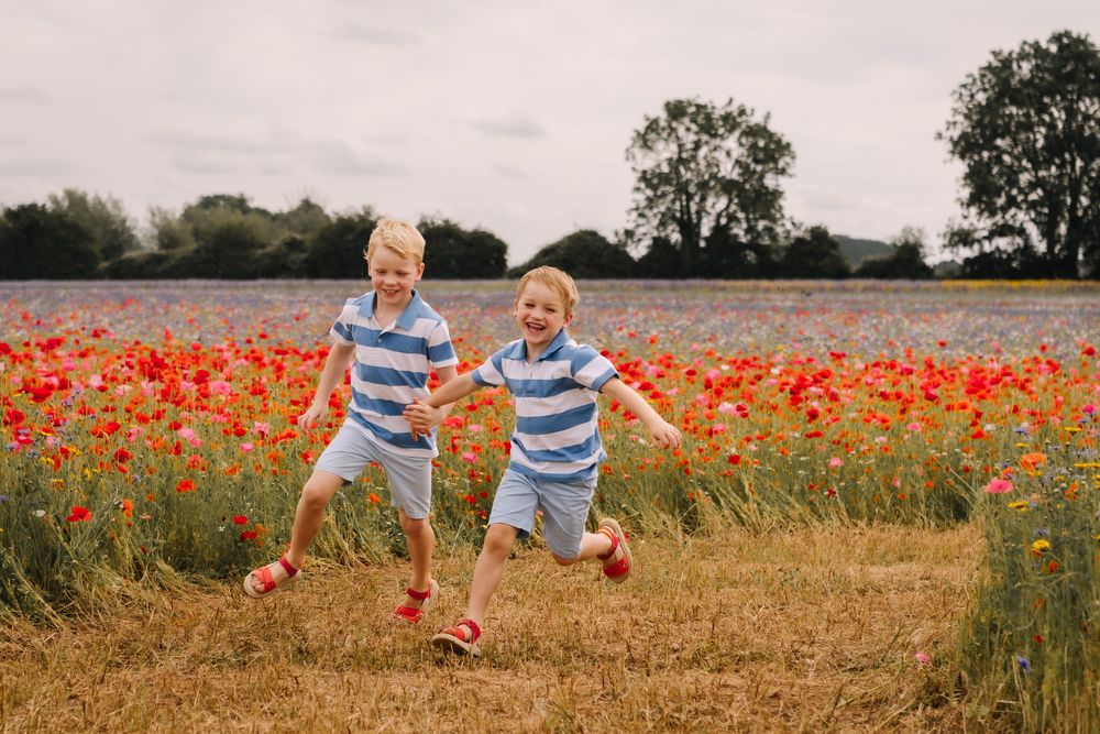 Two joyful boys in matching blue striped shirts run hand-in-hand through a vibrant red poppy field.