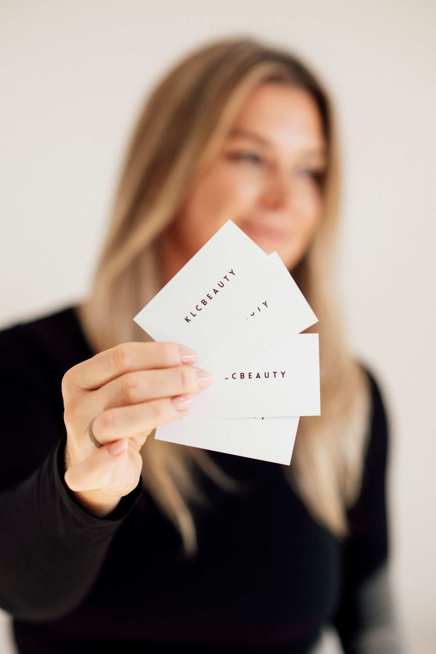 Woman in black holding up multiple white business cards against light background.