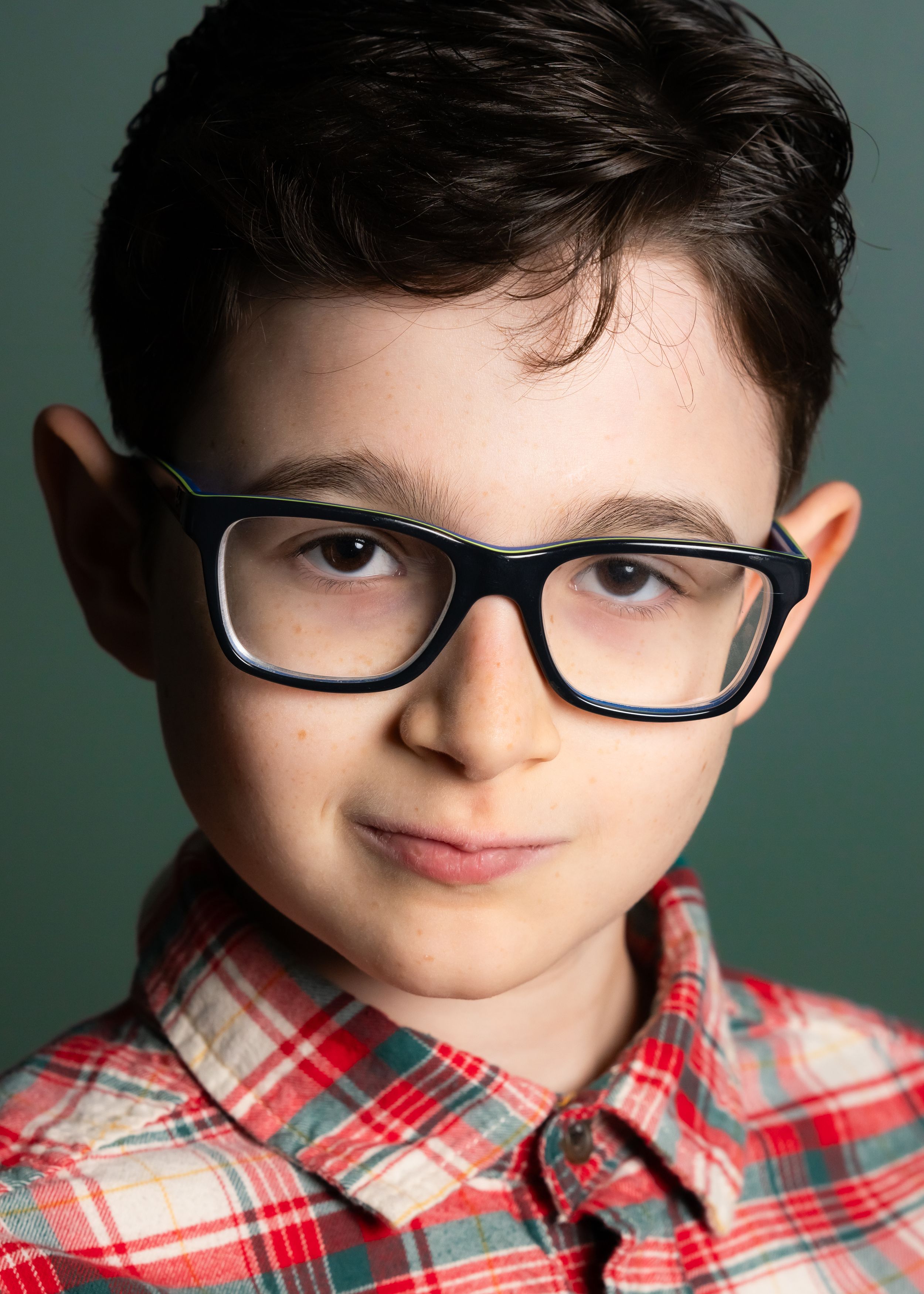A studio portrait with black glasses against a teal background.