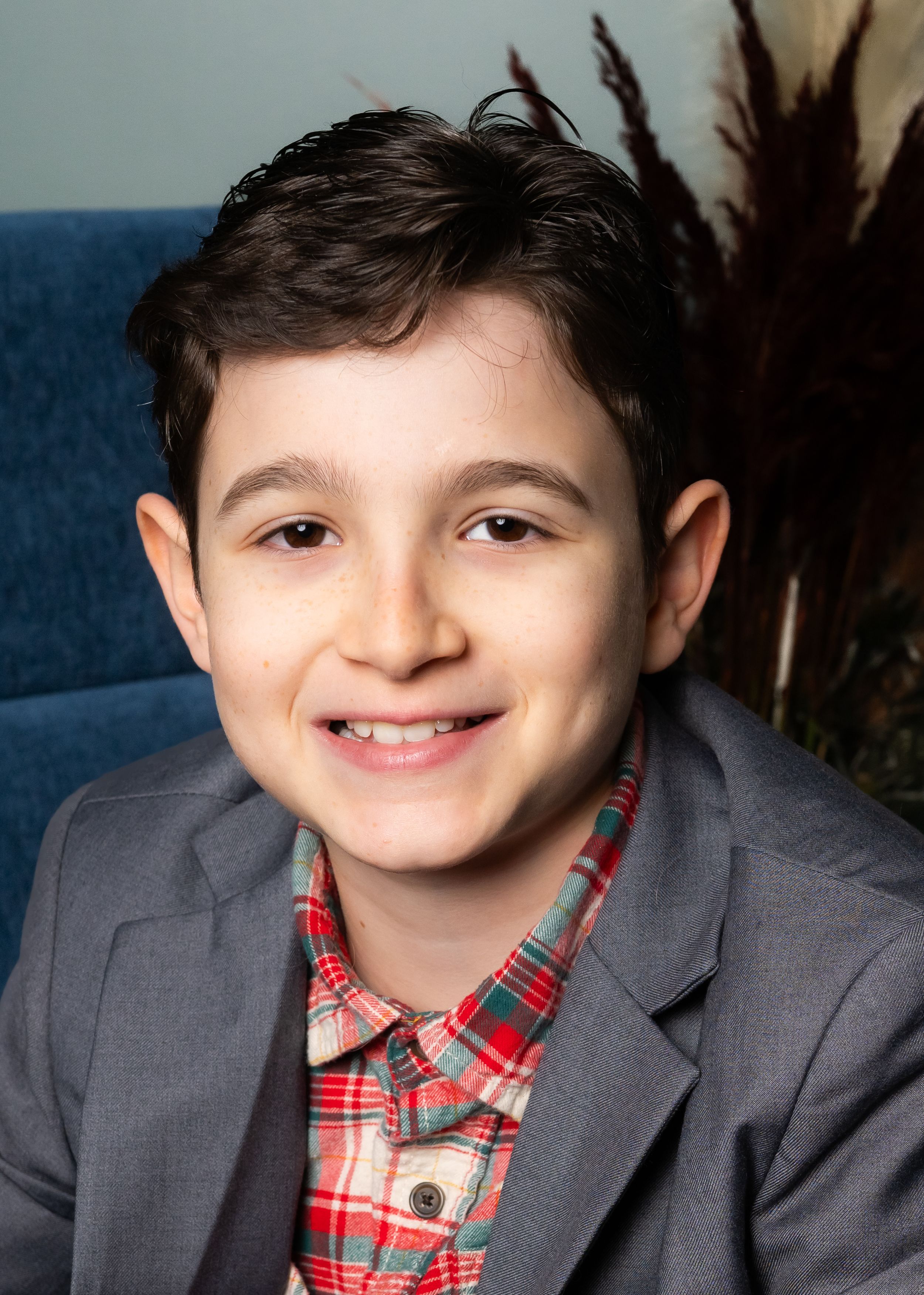 A portrait in plaid and gray blazer against a blue velvet backdrop.