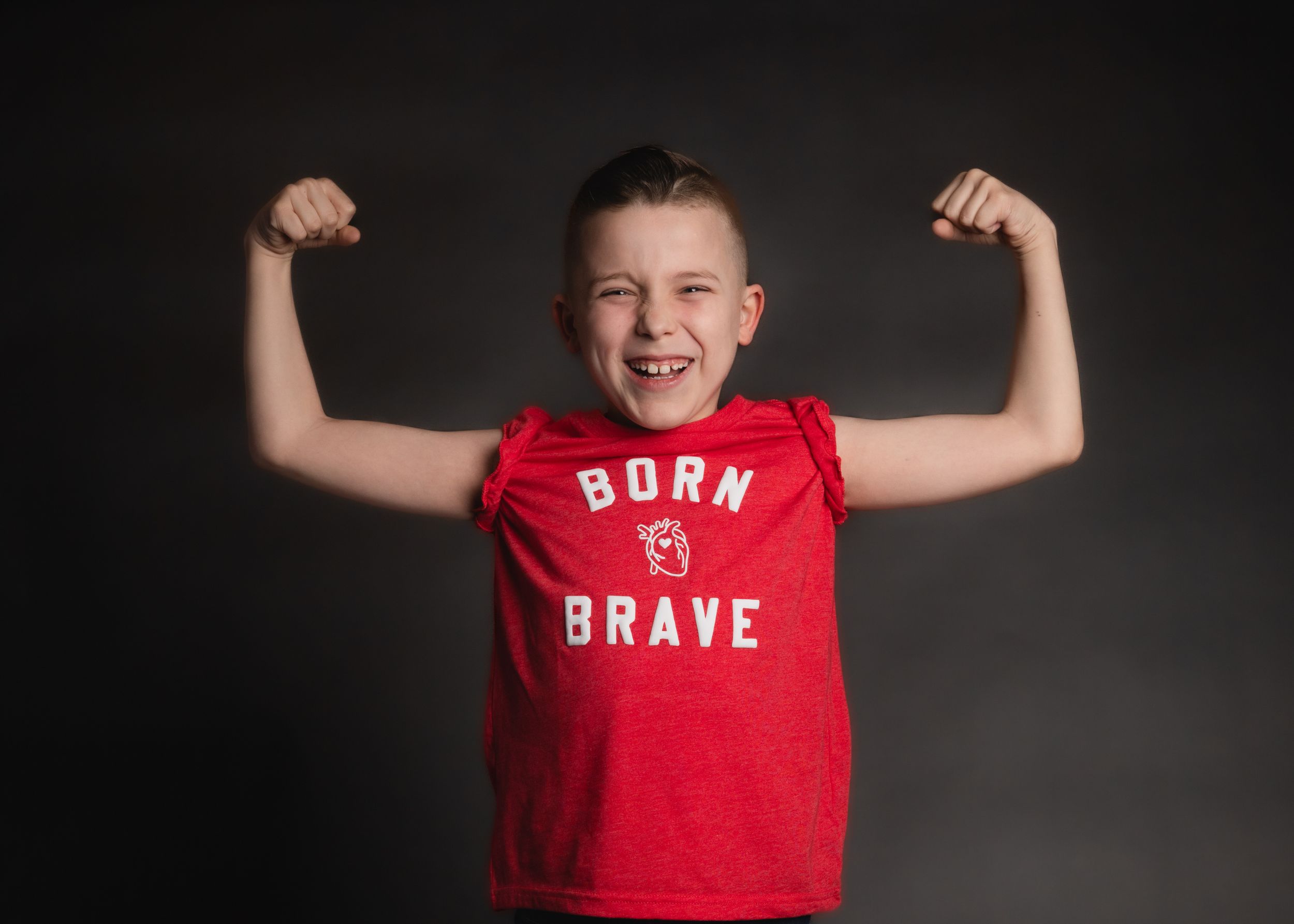 Red 'Born Brave' t-shirt worn while flexing arms against dark background.