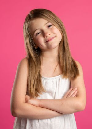 Studio portrait against pink background showing confident pose with crossed arms.