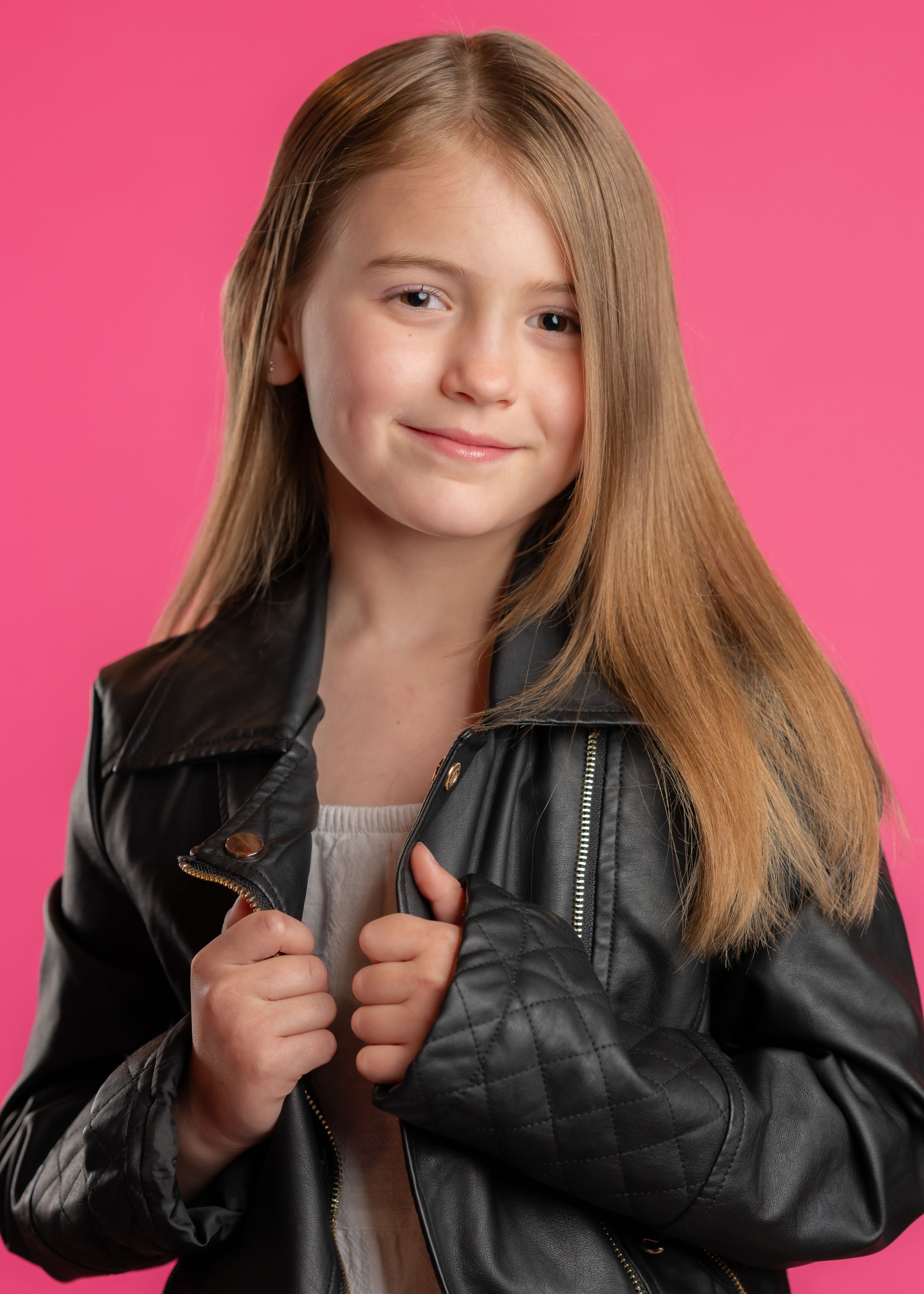 Portrait against pink background showing long straight hair and black leather jacket.