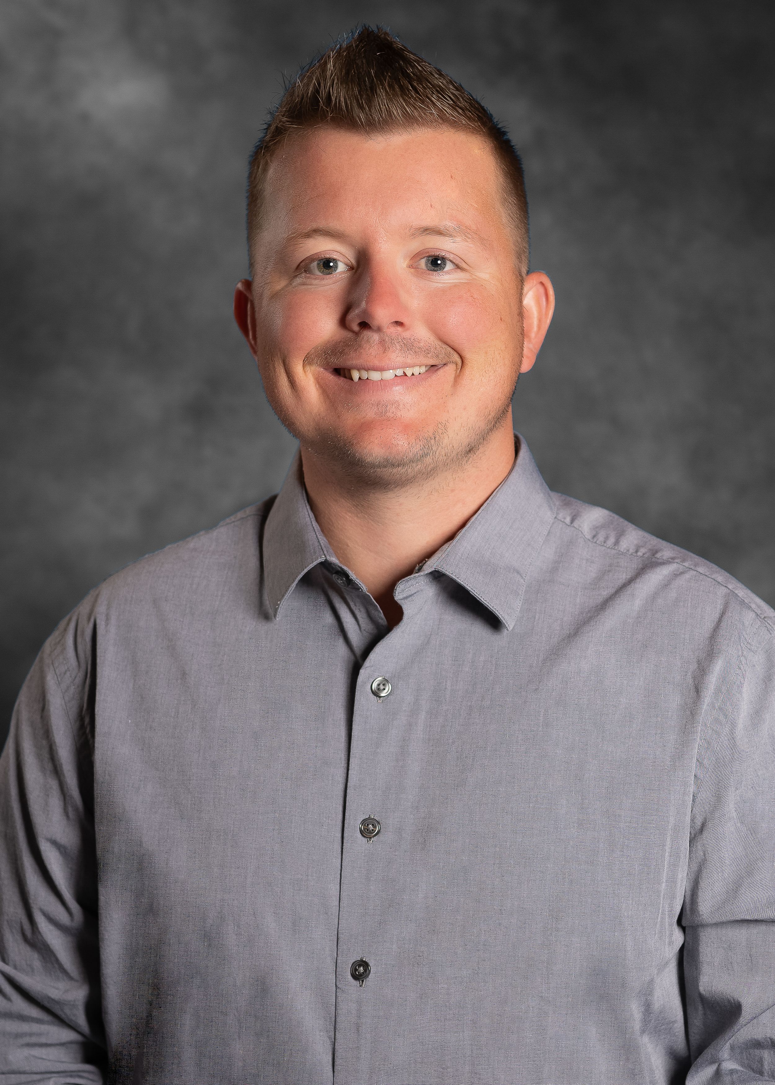 Professional portrait of person wearing gray dress shirt against gray backdrop.