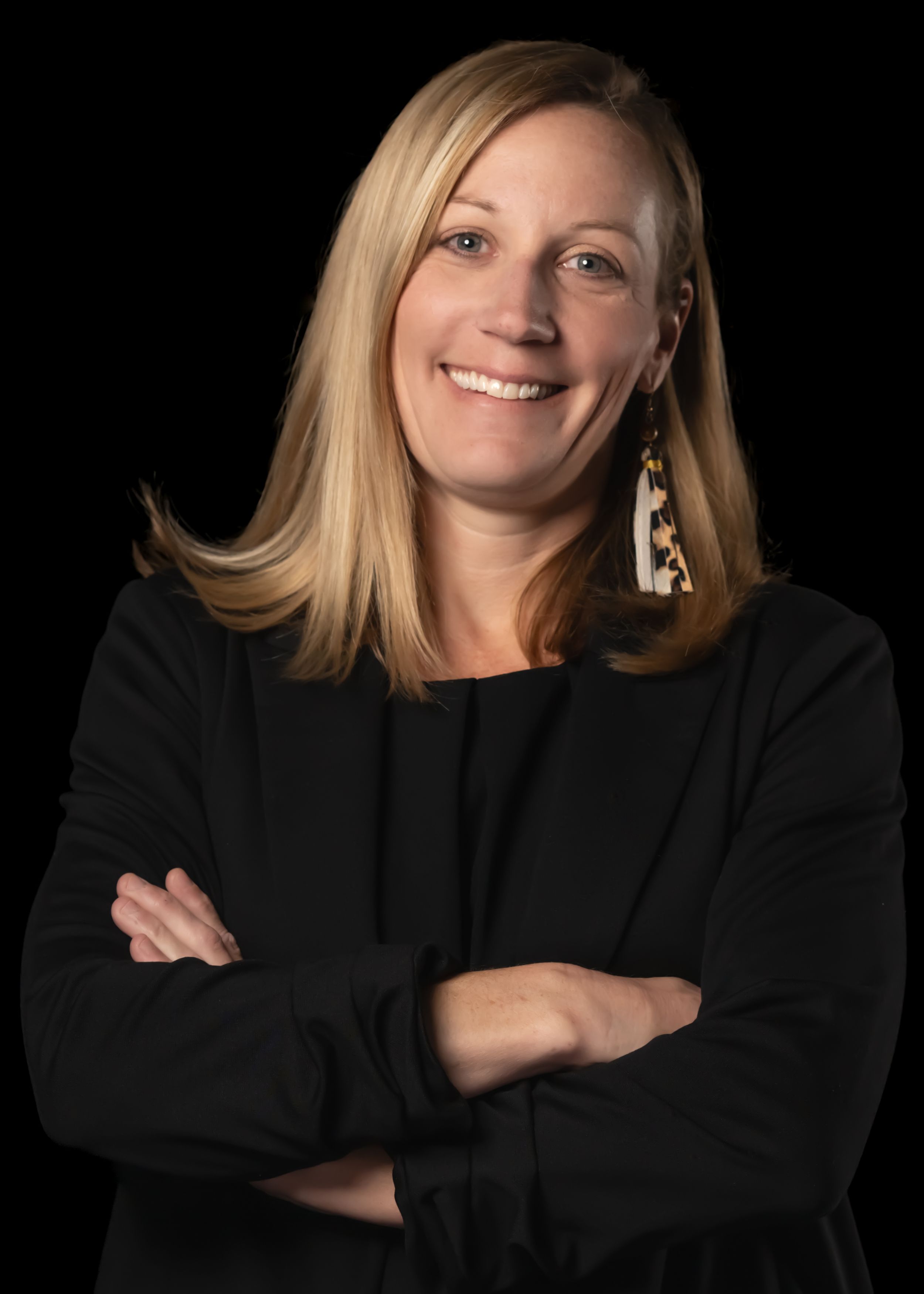 Professional headshot against black background wearing black blazer and statement earrings.