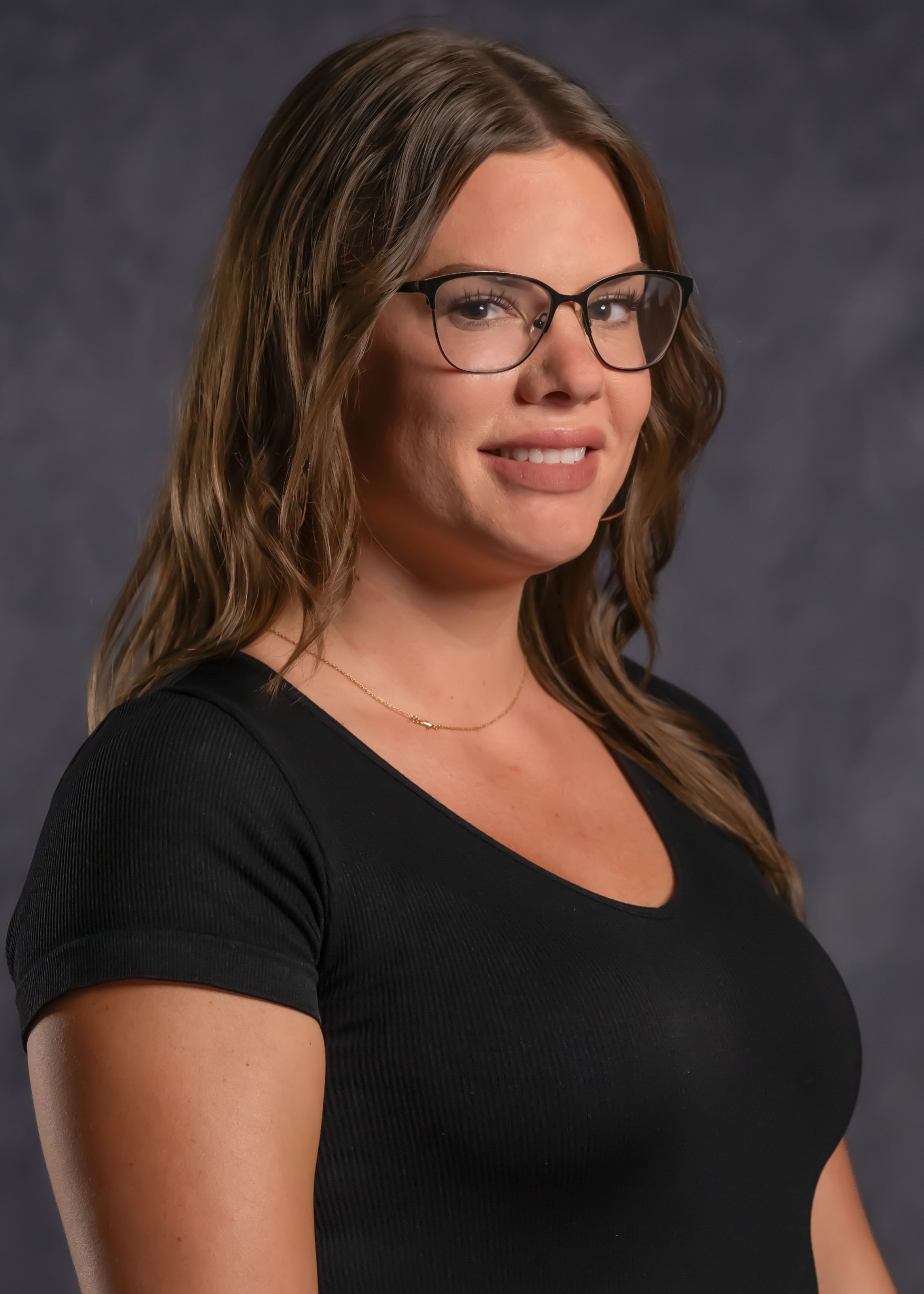 Professional portrait of woman in glasses wearing black top against gray backdrop.