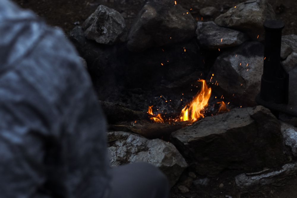 over-shoulder image of man sitting next to bonfire surrounded by rocks