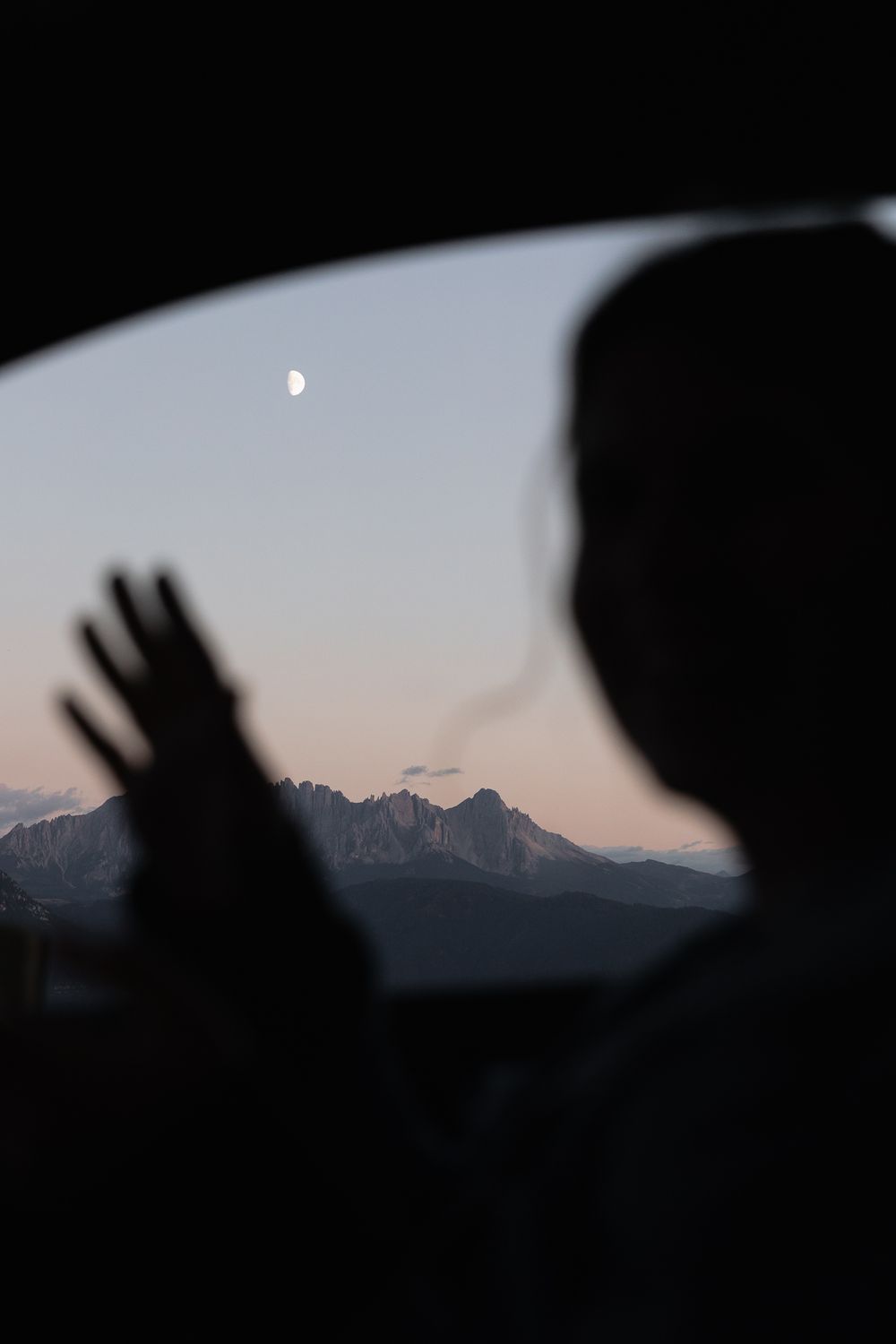 black silhouette of blurry person and hand with focus on pink mountains and moon in the background