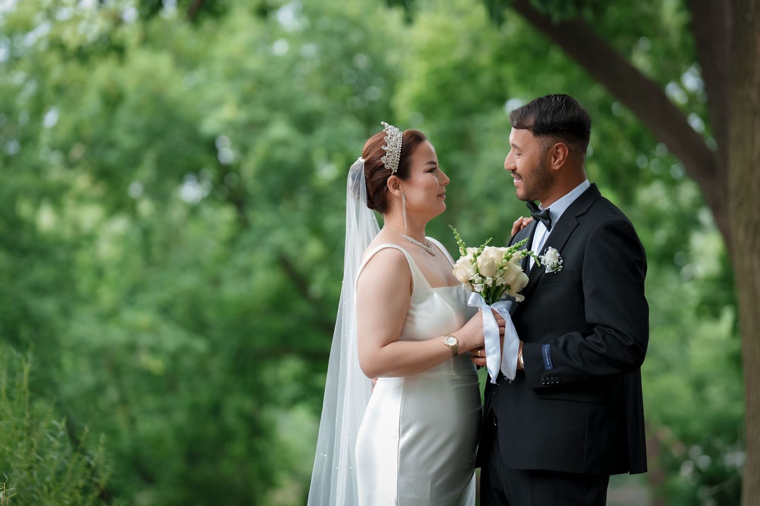 A couple in wedding attire shares a romantic moment in a lush green garden setting.