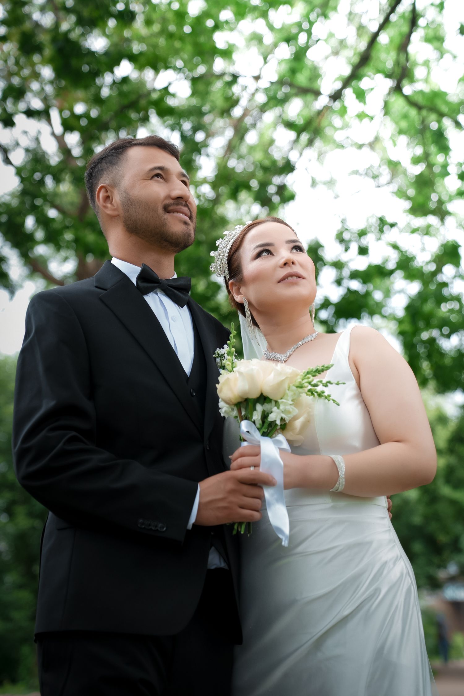 A romantic wedding couple shares intimate moments under green trees in a series of candid shots.