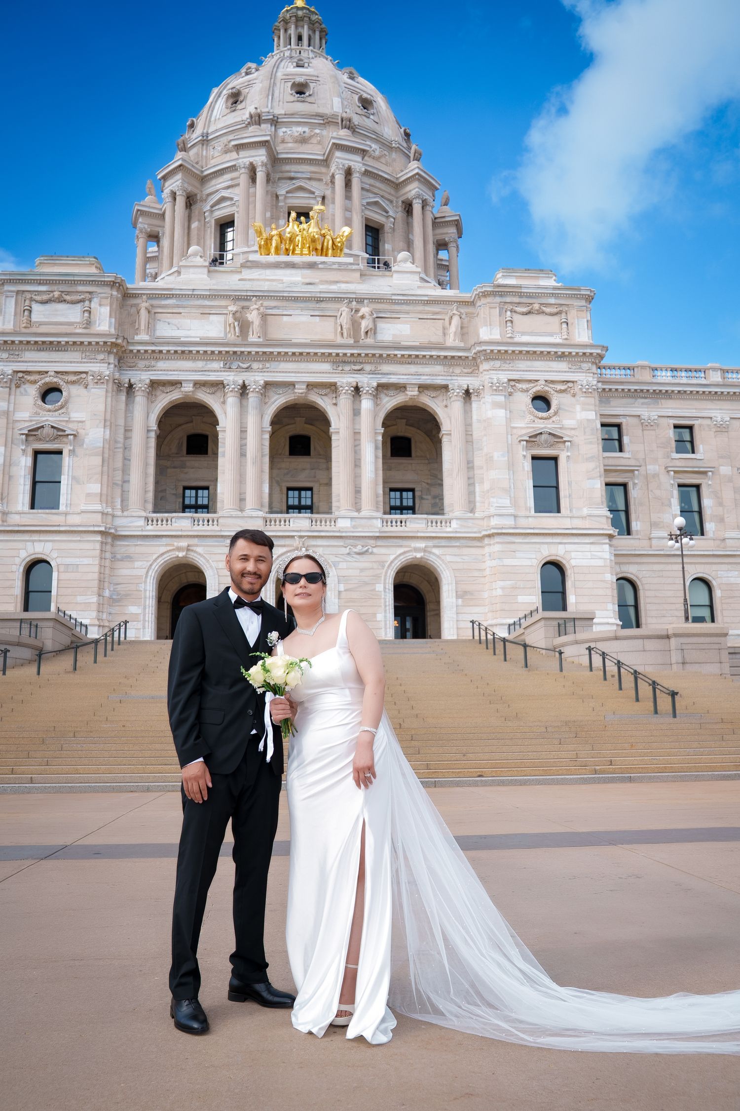 Wedding couple poses outside the Minnesota State Capitol building with its grand dome and architecture.