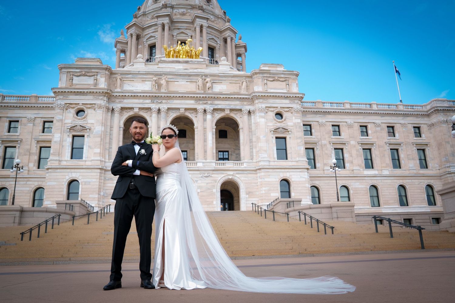 Wedding party poses outside the Minnesota State Capitol building with its grand neoclassical architecture and blue sky.