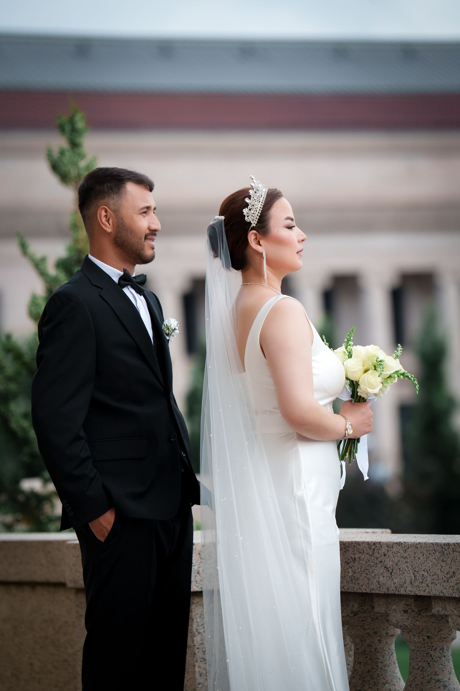 A bride and groom pose for artistic wedding portraits on a stone balcony in a romantic outdoor setting.