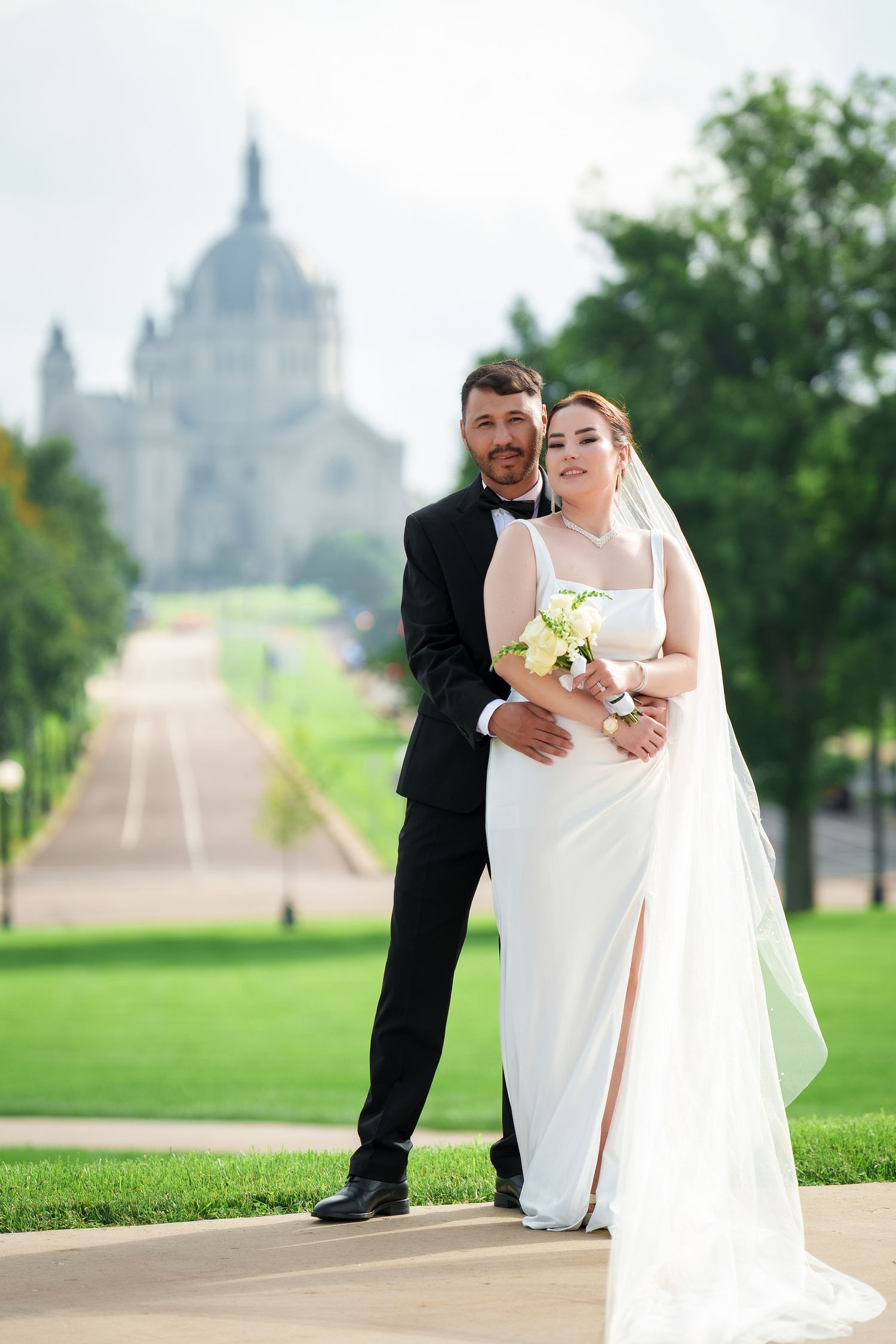 Wedding couple poses on path with Cathedral of Saint Paul in background on summer day in Minnesota.